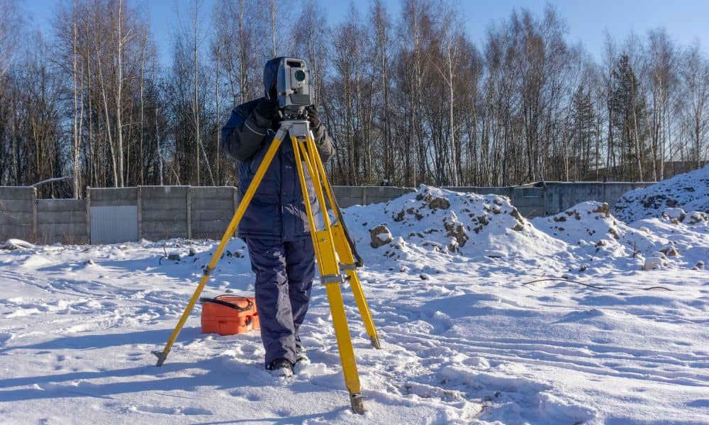 Surveyor conducting a construction staking survey on a snowy site using a total station
