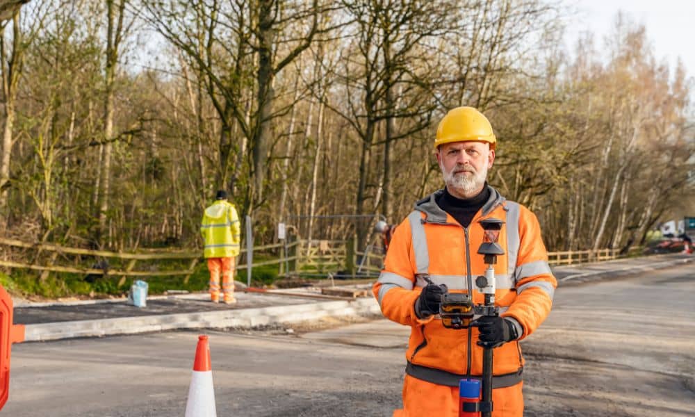Construction surveyor standing near traffic cones during a roadside construction survey, highlighting construction survey safety practices