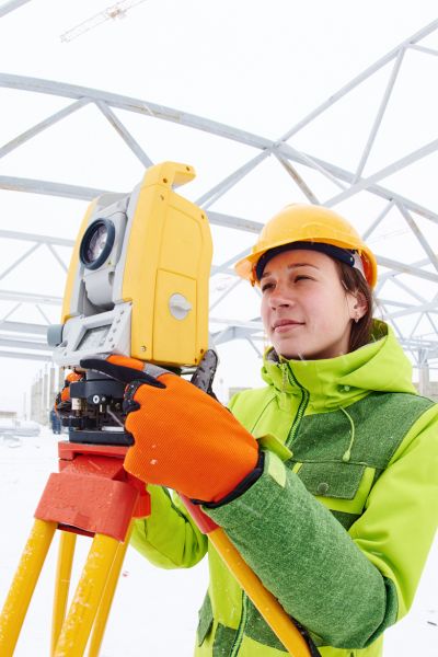 A licensed land surveyor using measurement equipment at a snowy job site to check property boundaries