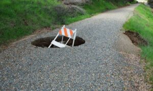Due diligence survey sinkhole road risk - ALTA SURVEY Minneapolis Sinkhole on a gravel road with warning sign showing why a due diligence survey is needed before construction