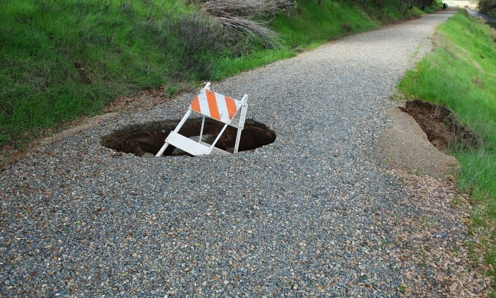 Sinkhole on a gravel road with warning sign showing why a due diligence survey is needed before construction
