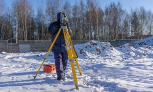Construction staking survey in winter - ALTA SURVEY Minneapolis Surveyor conducting a construction staking survey on a snowy site using a total station