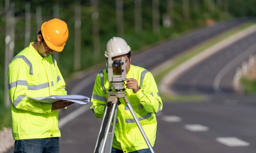 Roadside survey crew total station - ALTA SURVEY Minneapolis Survey crew performing land surveying near a roadway while wearing high-visibility safety gear