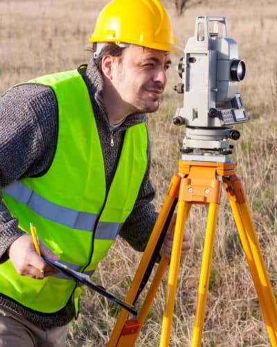 Surveyor using a total station to measure ground points and check property boundaries